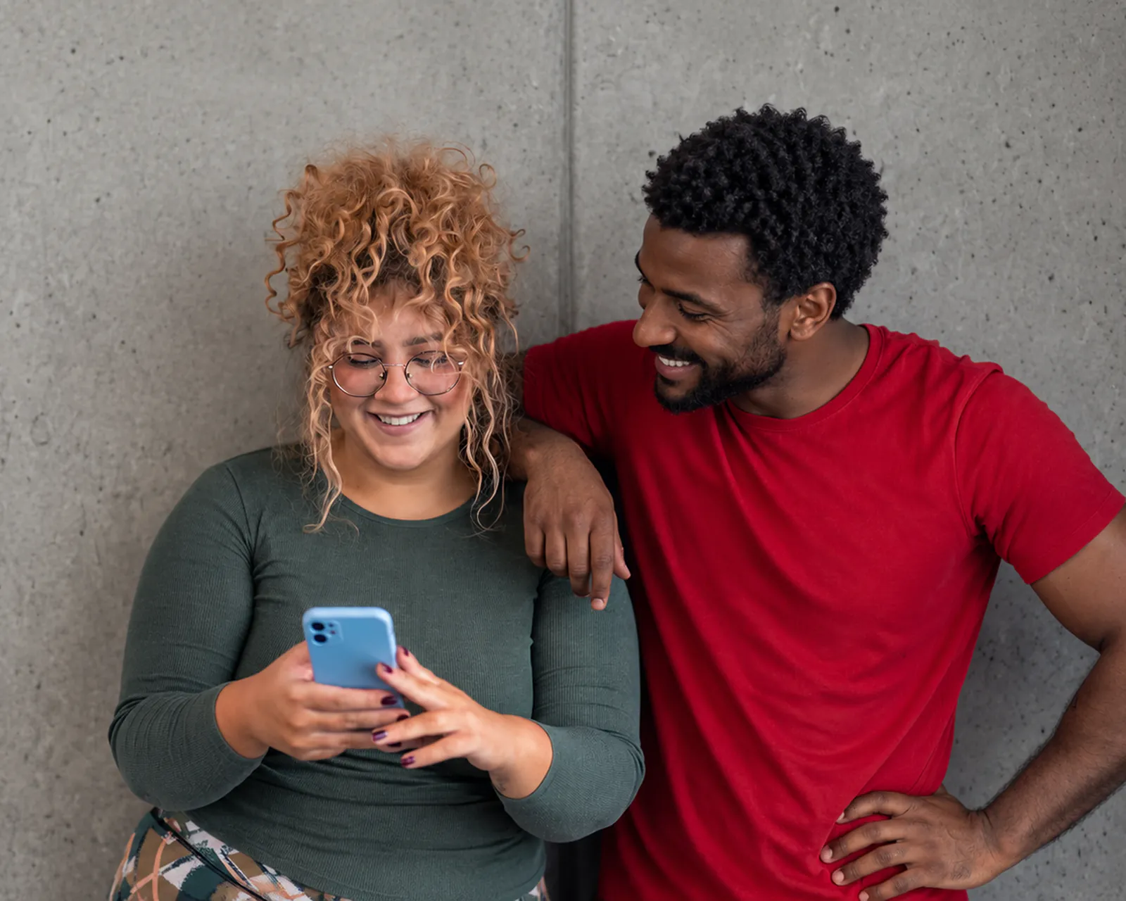 Smiling woman looking at her phone while a man in a red T-shirt leans on her shoulder